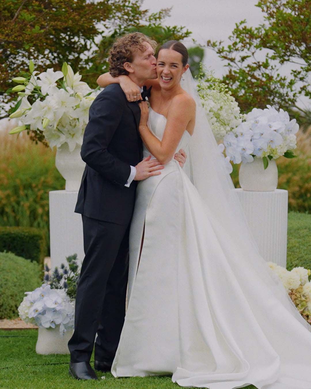 A bride laughing as her groom kisses her cheek, a still from a Sea of Love wedding film