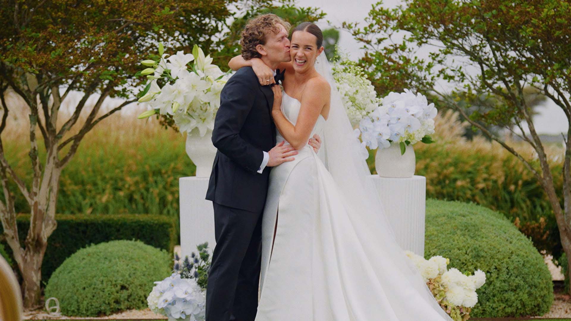 A groom kissing his bride's cheek at their wedding, captured on film by Sea of Love